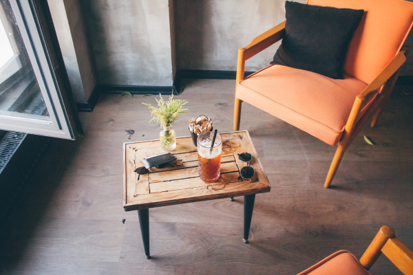 Iced coffee on a rustic wooden table next to a modern orange armchair in a cozy cafe.