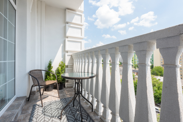 Modern apartment balcony featuring a bistro table, chair, and white stone balustrade overlooking a city.