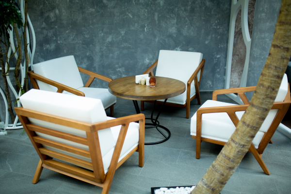 Four modern wooden armchairs with white cushions around a round table in a minimalist patio lounge.